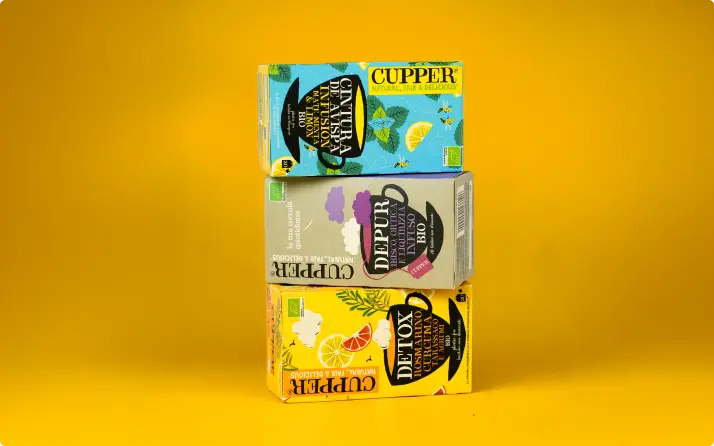 Cajas de infusiones ecológicas Cupper apiladas sobre un fondo amarillo.