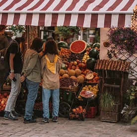 Personas comprando frutas y verduras frescas en un puesto de mercado.