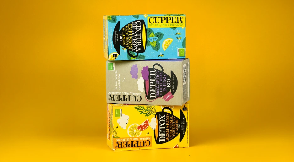 Cajas de infusiones ecológicas Cupper apiladas sobre un fondo amarillo.